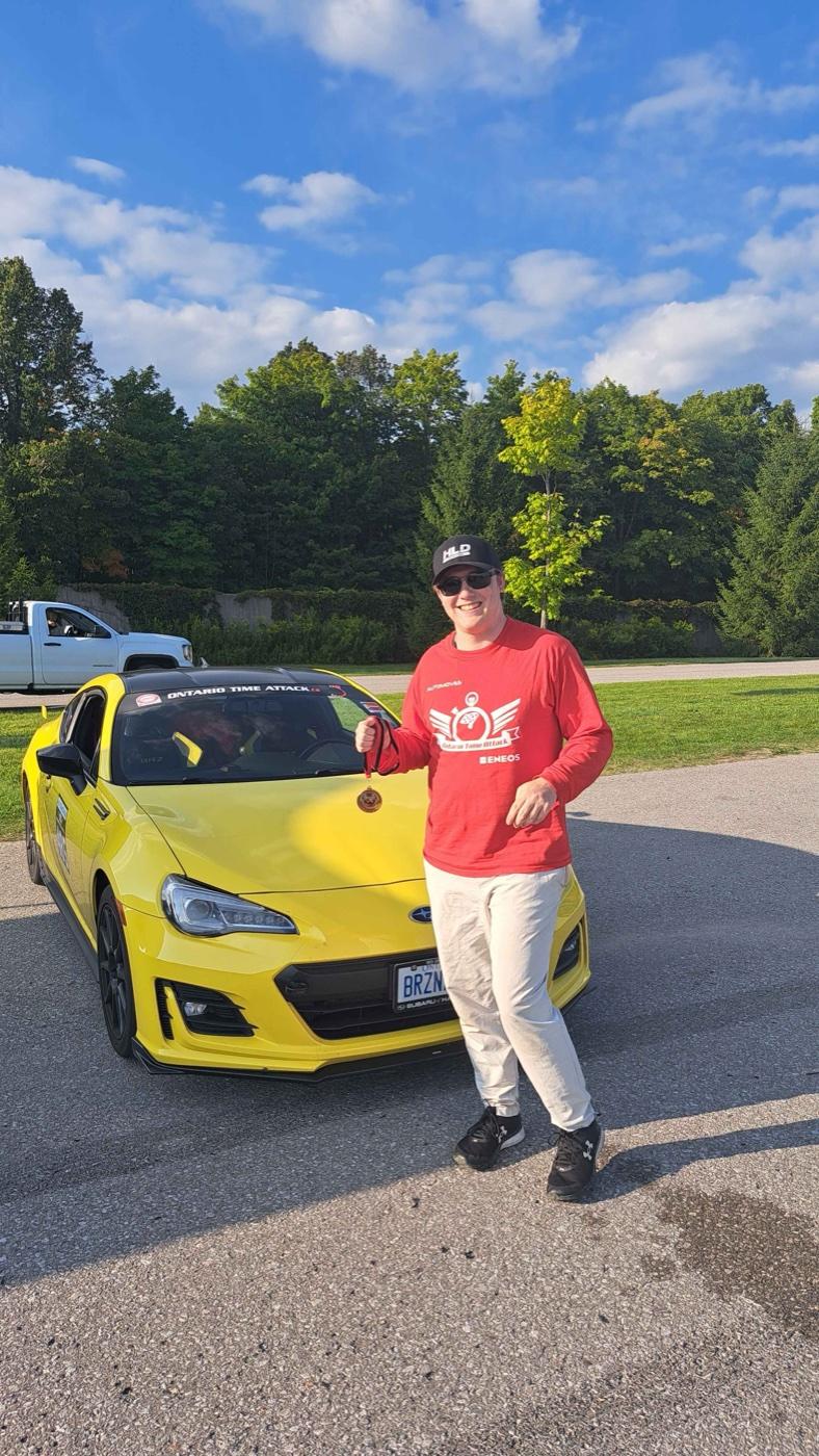 Dale with a podium medal beside his yellow BRZ at the track