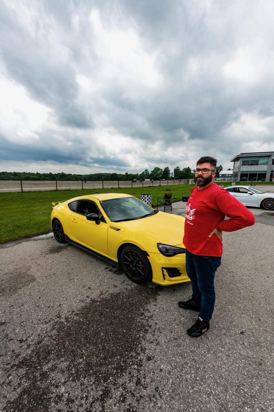Dale standing beside his yellow Subaru BRZ track car